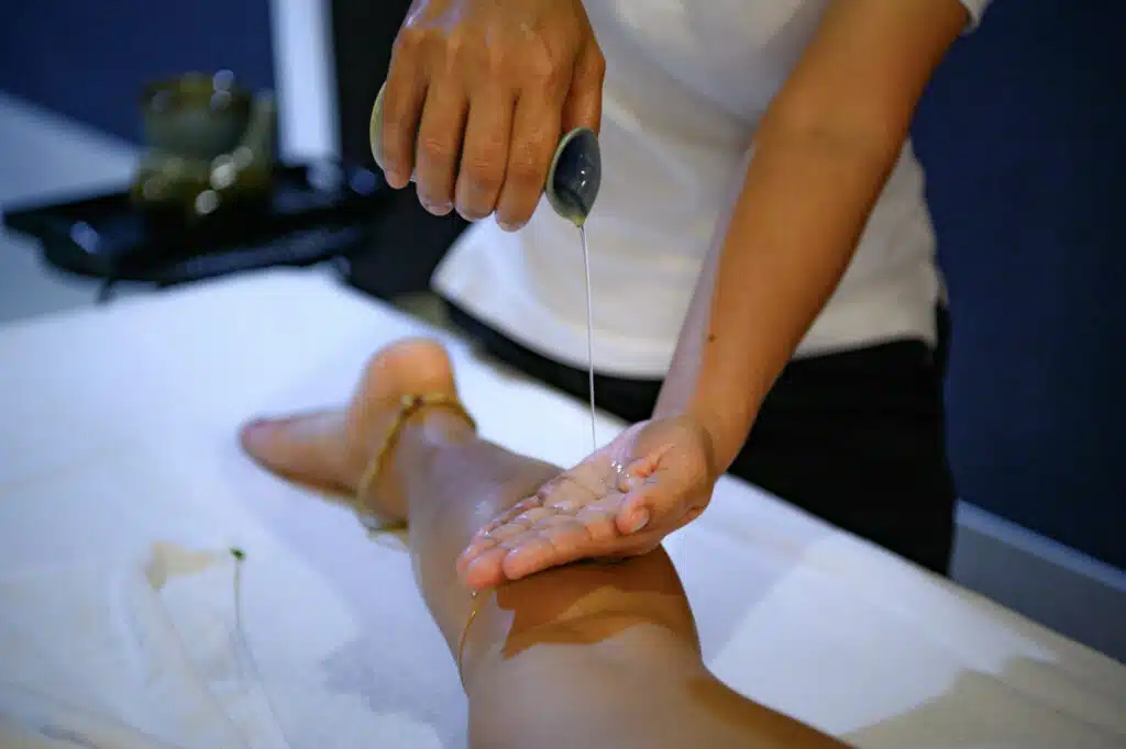 Aroma oil massage in Phuket: Therapist pouring aroma oil during a relaxing leg massage at a luxury spa